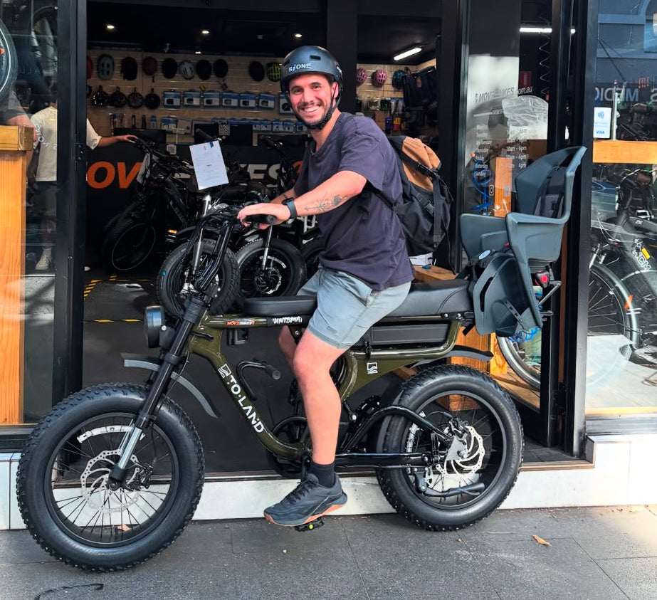 An electric bike with fat tyres, disc brakes, and a rear cargo rack. Accessories including a helmet, bike lock, and phone holder are displayed.