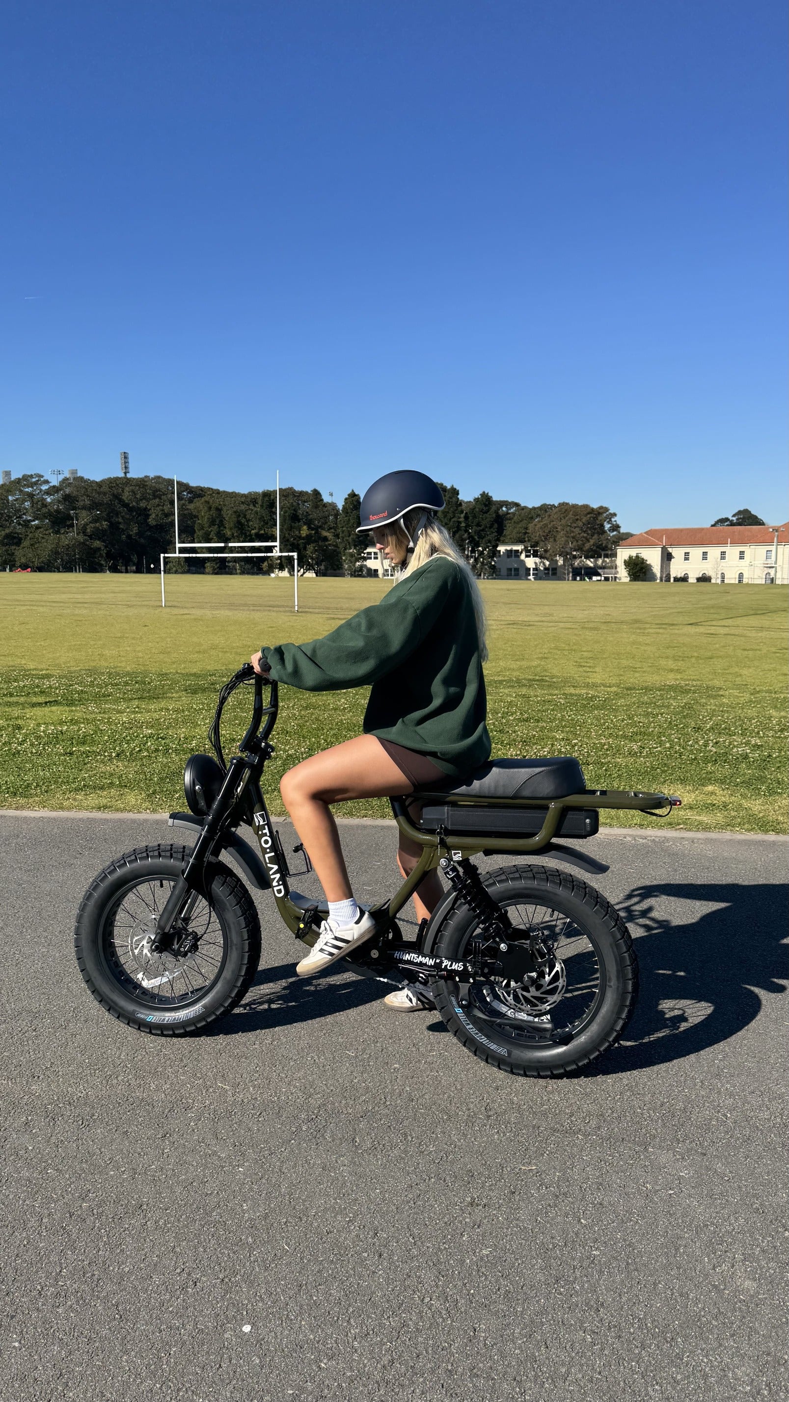 Person riding a electric bike on a road with a clear blue sky and grassy area in the background