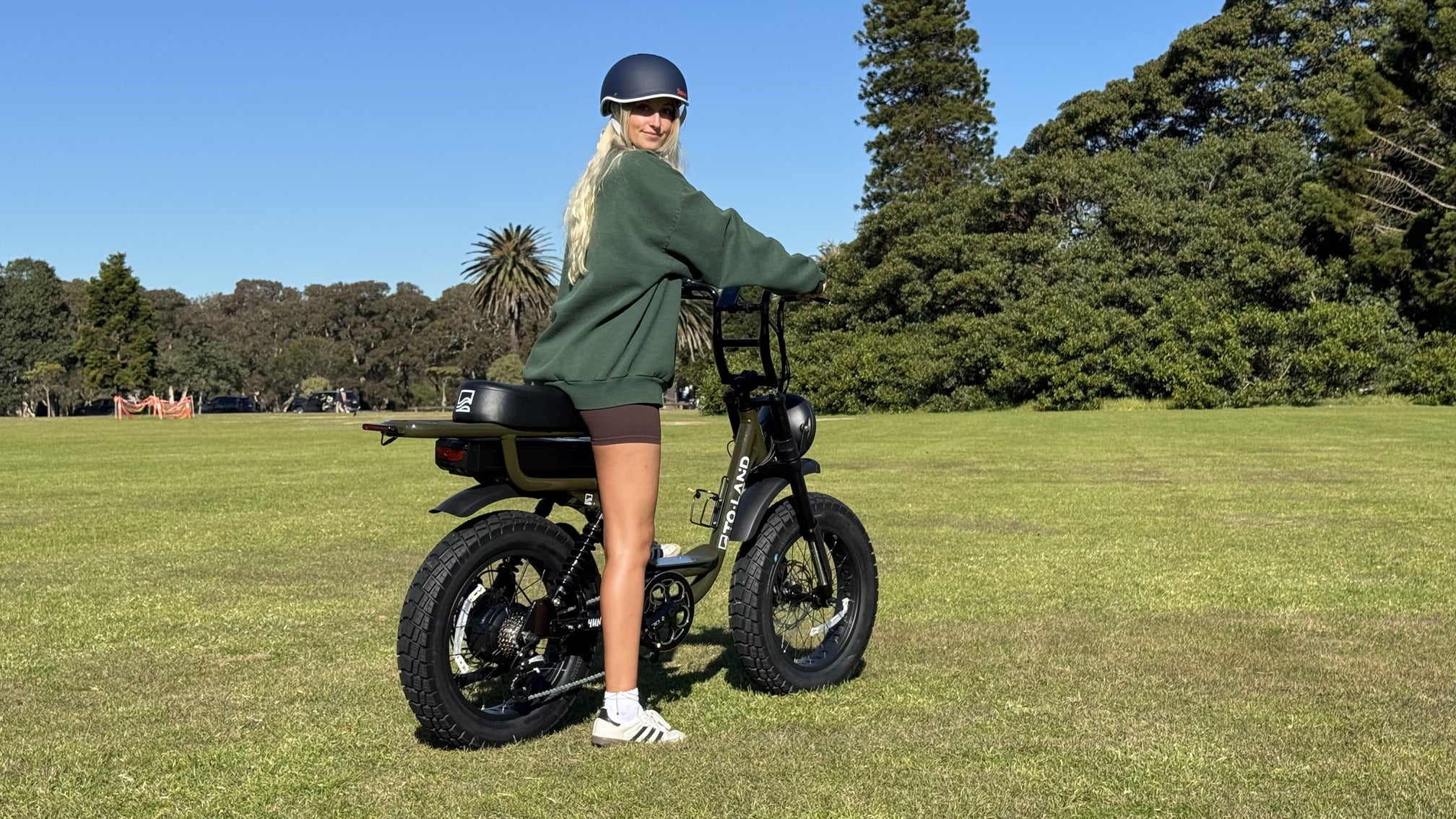 Person standing next to an electric bike on a grassy field with trees in the background
