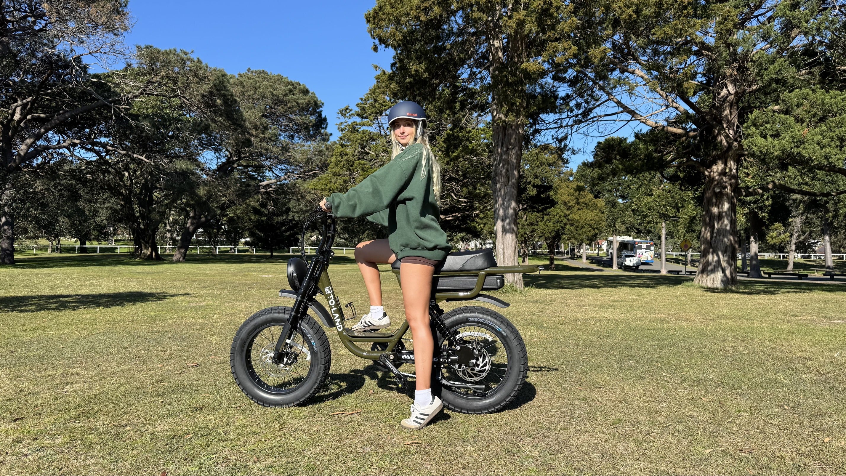Person on an electric bike in a park with trees and grass.