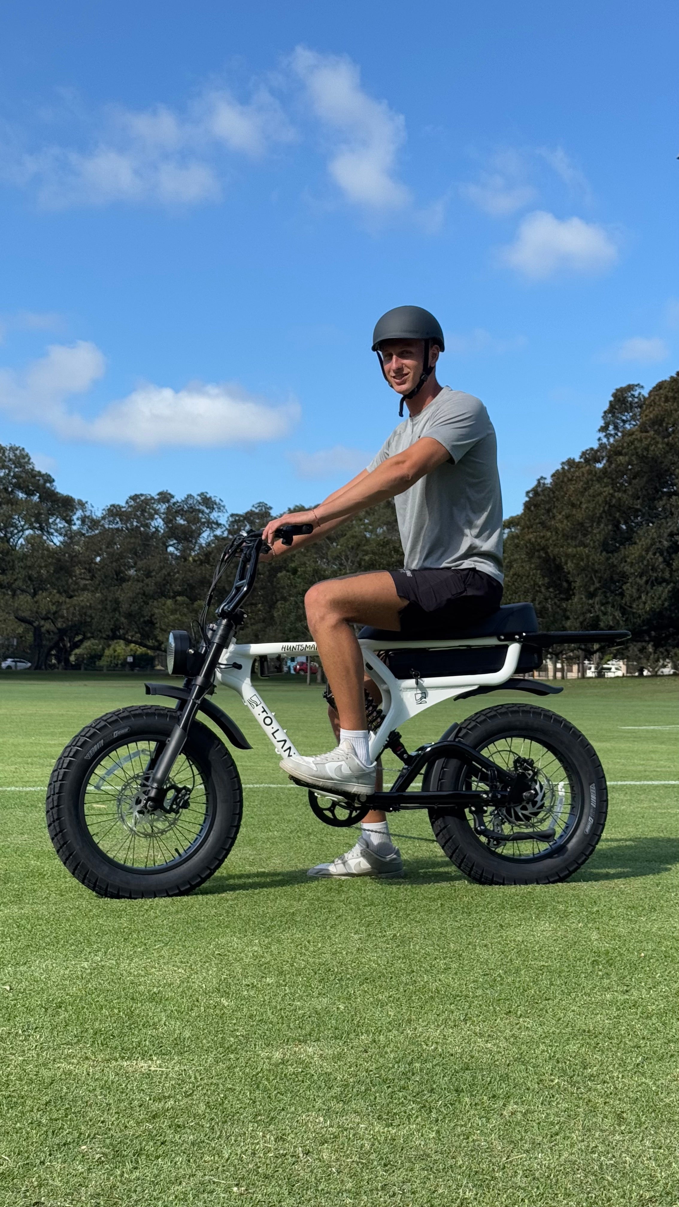Person on an electric bike in a park with trees and grass.