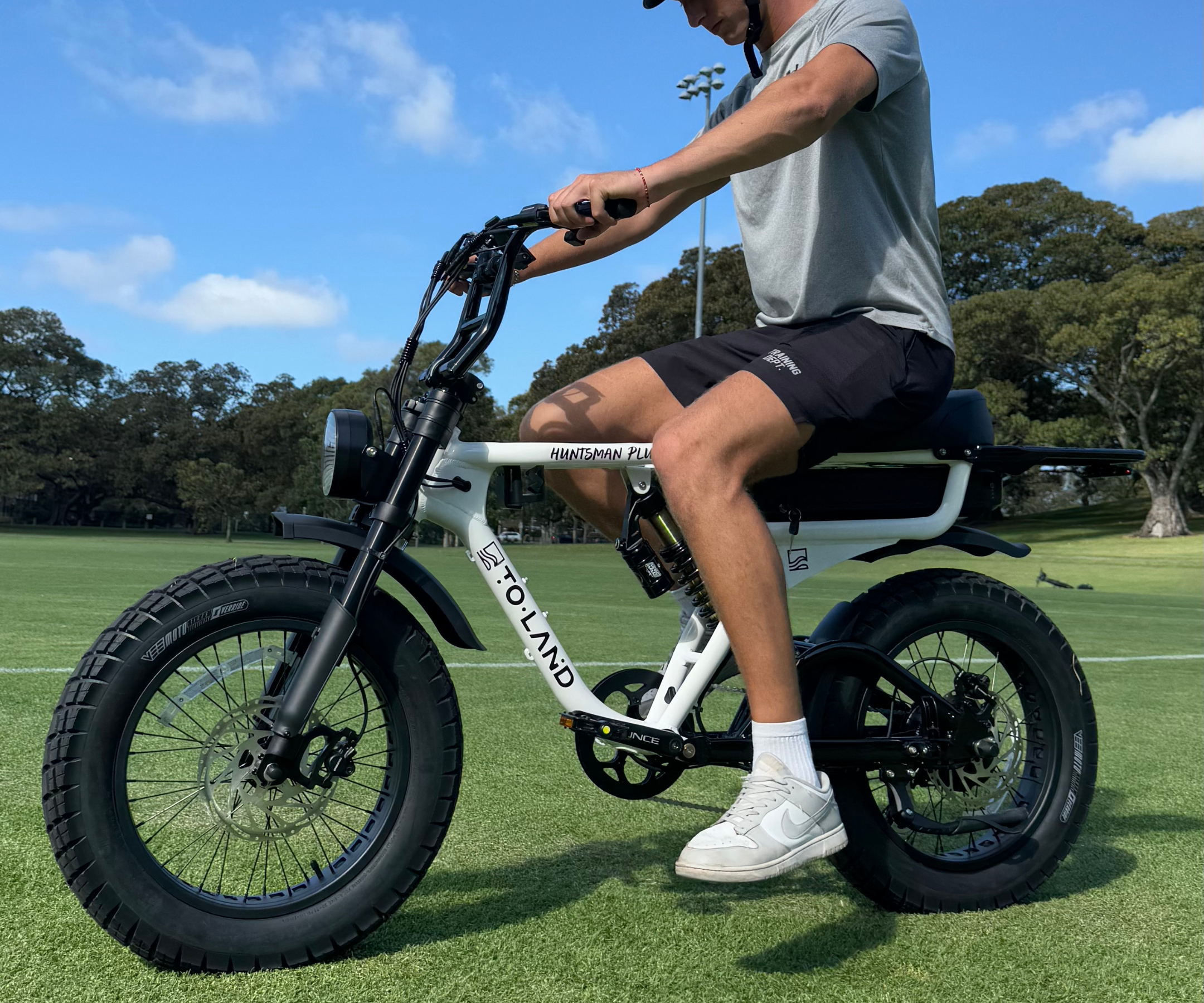 Person riding a white electric bike with large black tires on a grassy field.